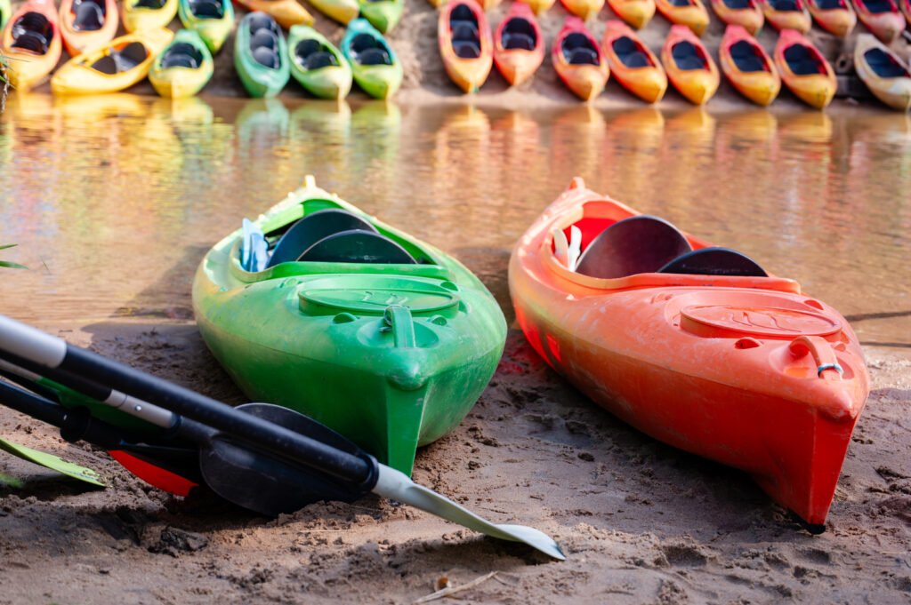 two kayaks on sandy riverbank with many colorful kayaks in backg