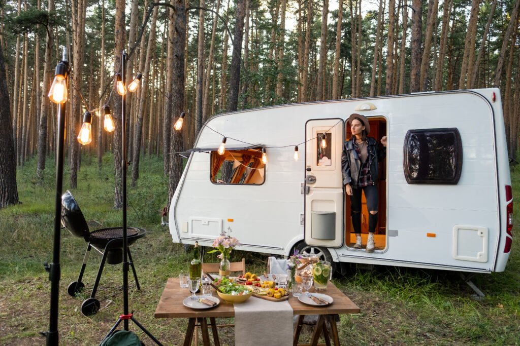 young woman in house on wheels among pinetrees and served table in front